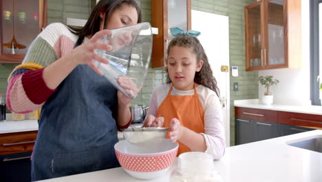 Happy-biracial-mother-and-daughter-preparing-dough-in-sunny-kitchen