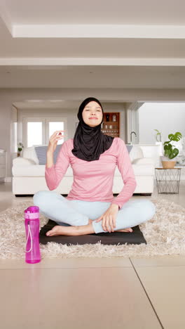 Vertical-video-of-focused-biracial-woman-in-hijab-practicing-yoga-at-home,-copy-space,-slow-motion