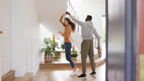 Happy-diverse-couple-dancing-and-smiling-in-sunny-hall-at-home,copy-space