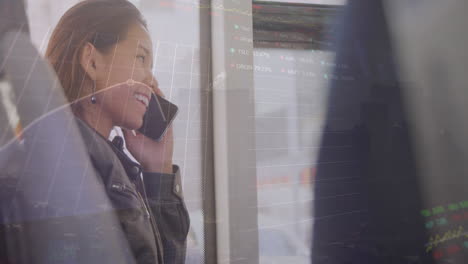 Animation-of-trading-board,-smiling-biracial-woman-talking-on-cellphone-while-travelling-in-bus