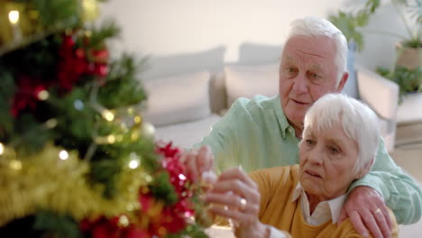 Happy-senior-caucasian-couple-decorating-christmas-tree-at-home,-slow-motion