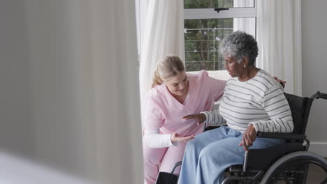 Smiling-caucasian-nurse-with-senior-african-american-woman-patient-in-wheelchair,-slow-motion