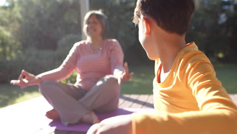 Happy-senior-biracial-grandmother-and-grandson-doing-yoga,-meditating-on-terrace,-slow-motion