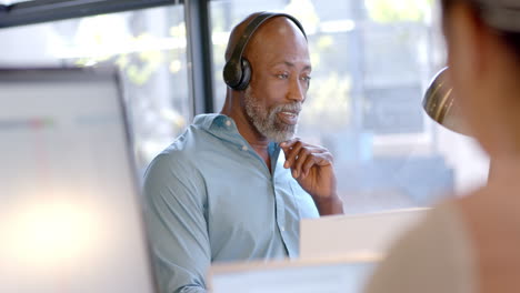 African-american-businessman-using-headphones-in-office-with-copy-space