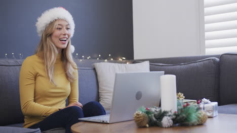 Happy-biracial-woman-wearing-santa-hat-using-laptop-for-christmas-video-call,-in-slow-motion