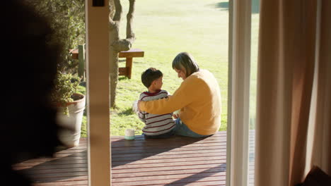 Happy-senior-biracial-grandmother-and-grandson-embracing-sitting-on-terrace,-slow-motion