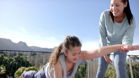 Happy-biracial-mother-and-daughter-practising-yoga-on-terrace-in-sunny-day,-slow-motion,-copy-space