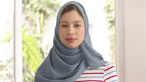Portrait-of-smiling-biracial-woman-in-hijab-at-home-with-copy-space,-slow-motion