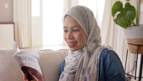 Glückliche-Biracial-Frau-Im-Hijab-Liest-Buch-Auf-Dem-Sofa-Zu-Hause-Mit-Kopierraum,-Zeitlupe