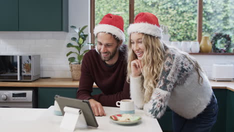 Vielfältiges-Paar-Mit-Weihnachtsmützen,-Das-Ein-Tablet-Für-Einen-Weihnachtsvideoanruf-In-Zeitlupe-Verwendet