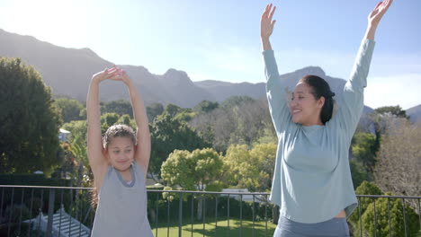 Happy-biracial-mother-and-daughter-practising-yoga-on-terrace-in-sunny-day,-slow-motion