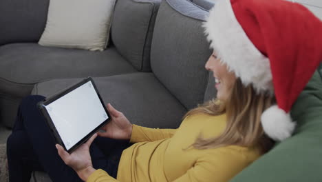 Happy-biracial-woman-wearing-santa-hat-using-tablet-at-christmas,-copy-space,-slow-motion