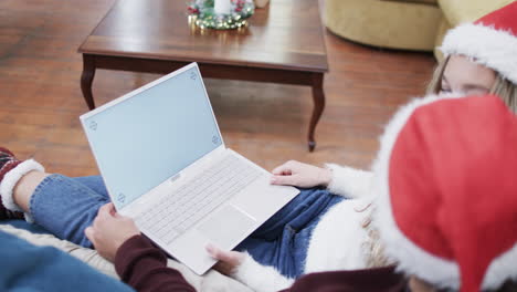 Vielfältiges-Paar-Mit-Weihnachtsmannmützen,-Das-Einen-Laptop-Mit-Kopierplatz-Auf-Dem-Bildschirm-In-Zeitlupe-Verwendet