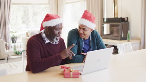 Glücklicher-Afroamerikanischer-Vater-Und-Sohn-In-Weihnachtsmützen-Mit-Laptop-Videoanruf,-Zeitlupe