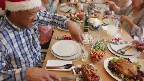 Happy-diverse-senior-male-and-female-friends-serving-food-at-christmas-dinner-table,-slow-motion