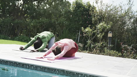 Happy-diverse-couple-exercising-yoga-in-sunny-garden,-slow-motion