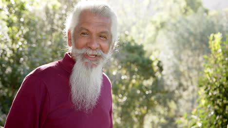 Portrait-of-senior-biracial-man-with-white-beard-smiling-in-sunny-nature,-copy-space,-slow-motion