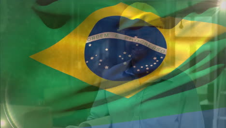 Animation-of-flag-of-brazil-waving,-biracial-engineer-wearing-helmet-walking-with-blueprints