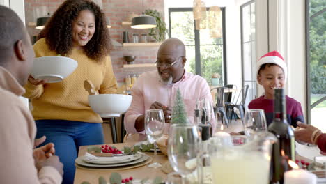 Glückliche-Afroamerikanische-Mutter-Serviert-Gerichte-Für-Mehrgenerationenfamilie-Am-Weihnachtstisch
