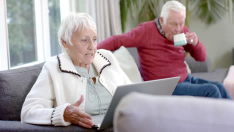 Glückliches-älteres-Kaukasisches-Paar,-Das-Zu-Hause-Mit-Einem-Laptop-Auf-Dem-Sofa-Sitzt-Und-Videoanrufe-In-Zeitlupe-Macht