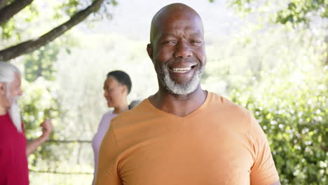 Glücklicher-Afrikanischer-Merican-Senior-Mann-Hält-Yoga-Matte,-Mit-Freunden-In-Sonniger-Natur,-Zeitlupe