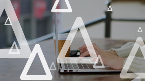 Animation-of-multiple-triangles-over-cropped-hands-of-caucasian-woman-working-on-laptop-in-cafes