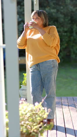 Vertical-video-of-happy-senior-biracial-woman-drinking-coffee-on-terrace,-slow-motion