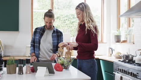 Happy-diverse-couple-preparing-dinner-in-kitchen-using-tablet-at-home,-in-slow-motion