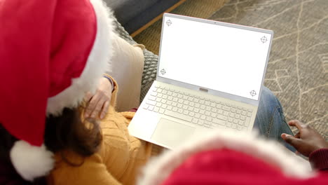 Happy-diverse-couple-in-christmas-hats-using-laptop-with-copy-space-screen,-slow-motion