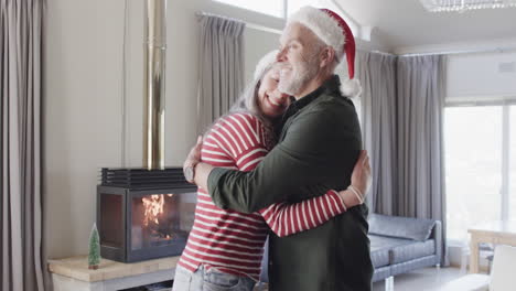 Middle-aged-caucasian-couple-in-santa-hats-cuddling-at-christmas-at-home,-slow-motion