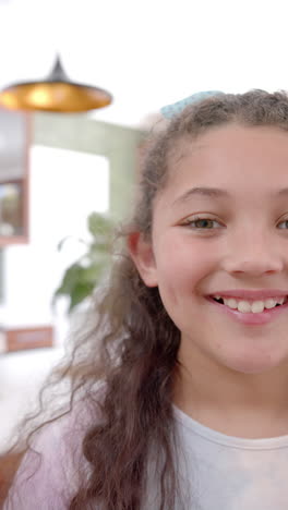 Vertical-video-of-half-face-of-happy-biracial-girl-with-long,-curly-hair-smiling-in-sunny-kitchen