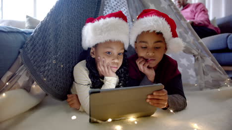 African-american-brother-and-sister-in-christmas-hats-using-tablet-in-blanket-tent,-slow-motion