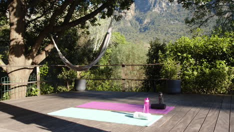 Zwei-Yogamatten,-Wasserflaschen-Und-Handtücher-An-Deck-Im-Sonnigen-Garten,-Kopierraum,-Zeitlupe
