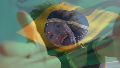Animation-of-flag-of-brazil-waving-over-biracial-woman-talking-selfie-video-with-camera-at-beach