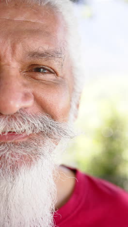 Vertical-video-half-portrait-of-happy-senior-biracial-man-with-white-beard-out-in-sun,-slow-motion