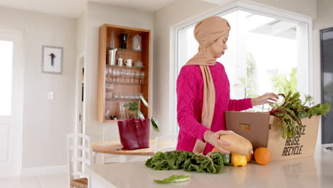 Glückliche-Biracial-Frau-Im-Hijab-Mit-Lebensmitteleinkauf-In-Der-Küche-Zu-Hause-Mit-Kopierraum,-Zeitlupe
