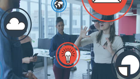 Animation-of-icons-over-diverse-woman-wearing-vr-headset-giving-feedback-to-coworkers-in-office