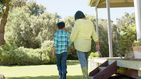 Happy-biracial-grandmother-and-grandson-walking-in-sunny-garden,-slow-motion