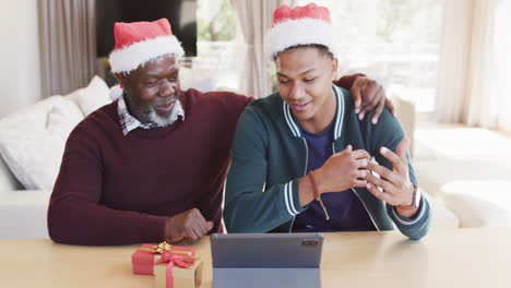 Feliz-Padre-Afroamericano-E-Hijo-Adulto-Con-Sombreros-De-Navidad-Con-Videollamada-De-Tableta,-Cámara-Lenta
