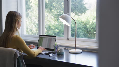 Biracial-Frau,-Die-Zu-Hause-Mit-Smartphone-Und-Laptop-Am-Schreibtisch-Sitzt,-Zeitlupe,-Kopierraum