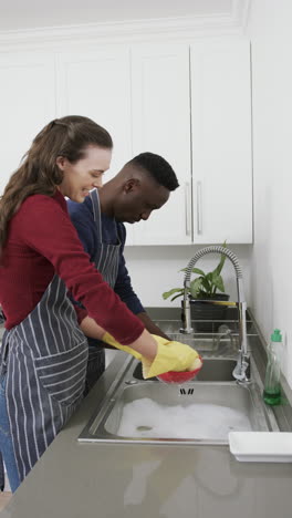 Happy-diverse-couple-smiling-and-washing-dishes-in-kitchen,-slow-motion,-copy-space