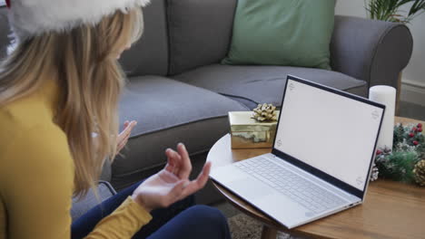 Happy-biracial-woman-wearing-santa-hat-using-laptop-at-christmas,-copy-space,-slow-motion