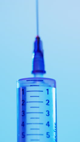 Vertical-video-of-laboratory-syringe-with-copy-space-on-blue-background