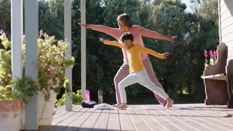Senior-biracial-grandmother-and-grandson-doing-yoga-and-stretching-on-terrace-at-home,-slow-motion
