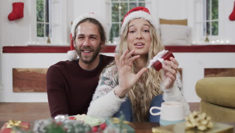 Happy-diverse-couple-wearing-santa-hats-having-christmas-video-call-at-home,-in-slow-motion