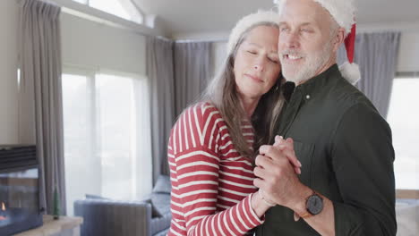 Middle-aged-caucasian-couple-in-santa-hats-dancing-at-christmas-at-home,-slow-motion