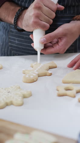 Vertical-video-of-midsection-of-caucasian-man-decorating-christmas-cookies,-slow-motion