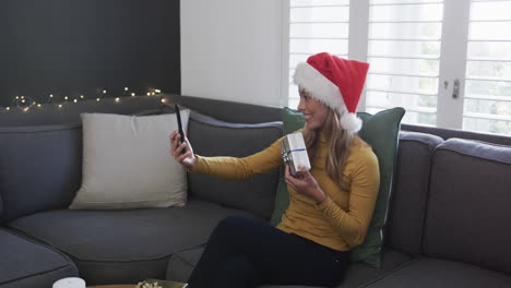 Happy-biracial-woman-wearing-santa-hat-using-smartphone-for-christmas-video-call,-in-slow-motion