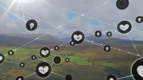 Animation-of-connected-icons-over-aerial-view-of-green-landscape-against-mountains-and-cloudy-sky