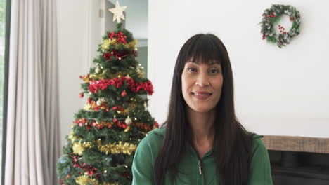 Portrait-of-happy-biracial-woman-smiling-by-christmas-tree-at-home,-copy-space,-slow-motion